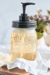 mason jar soap dispenser with pale amber liquid soap, and a black pump lid.