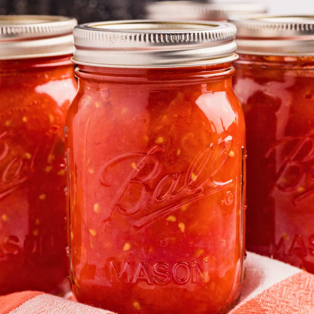 jars of canned crushed tomatoes on red and white tablecloth.