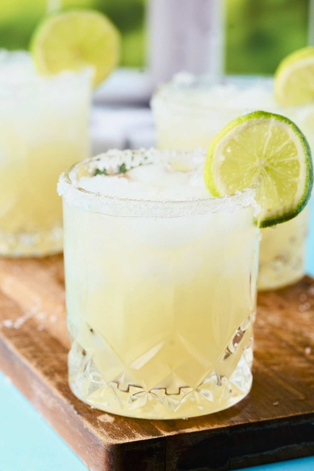 salt-rimmed key lime margaritas with lime slice on wooden board.