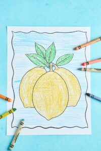 finished lemon coloring page with three yellow lemons, green leaves, and blue background with crayons scattered on sides.