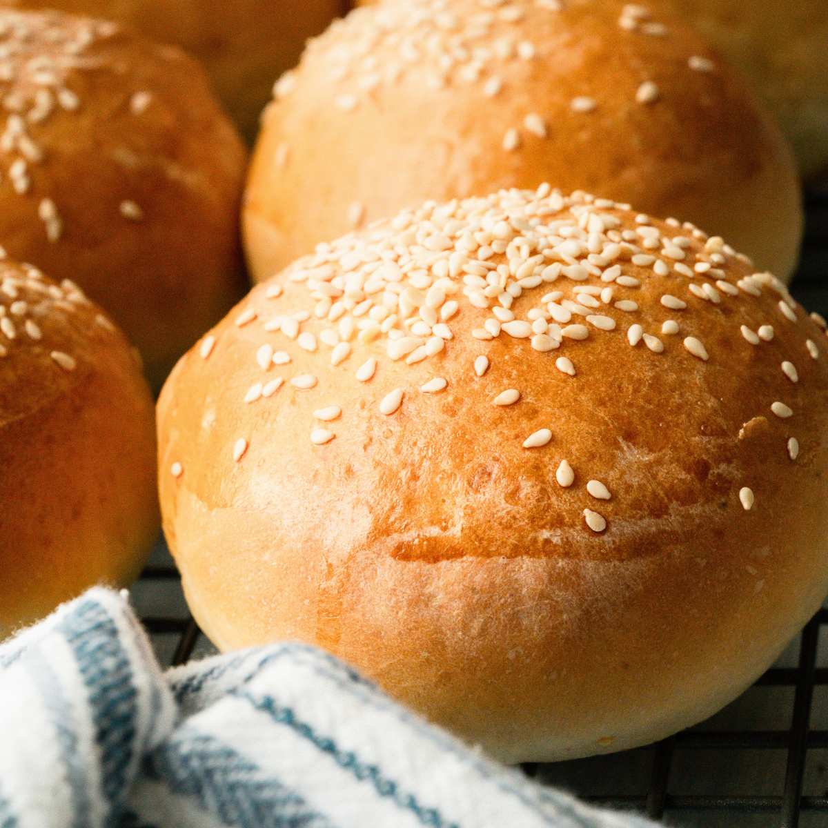 burger buns topped with sesame seeds with blue striped towel in front.