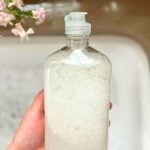hand holding clear bottle of liquid dish soap over bubbly sink.
