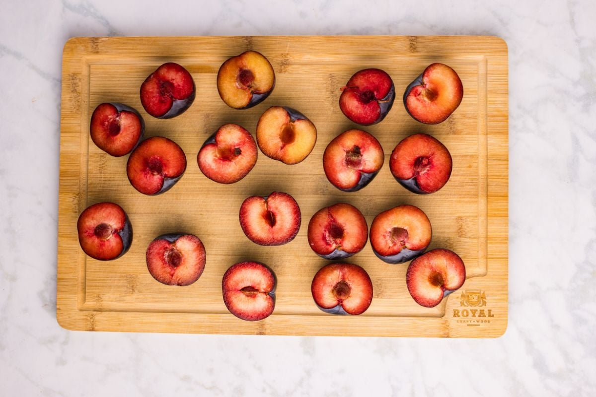Halved plums laid out on a wooden cutting board.