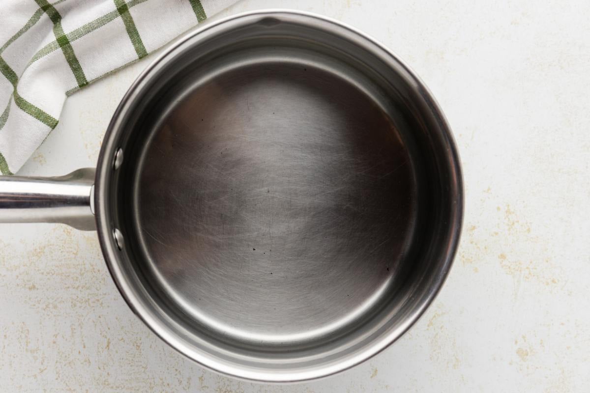 Empty saucepan on a counter next to a green checked towel.