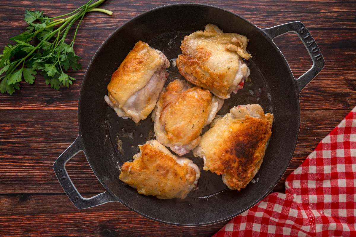 hicken thighs searing in a cast iron skillet.