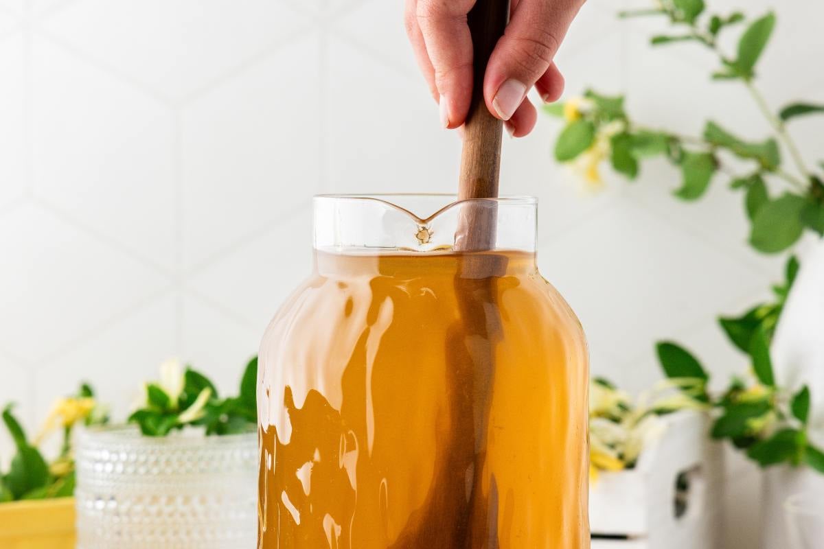 Wooden spoon stirring strained honeysuckle tea in a glass jar.