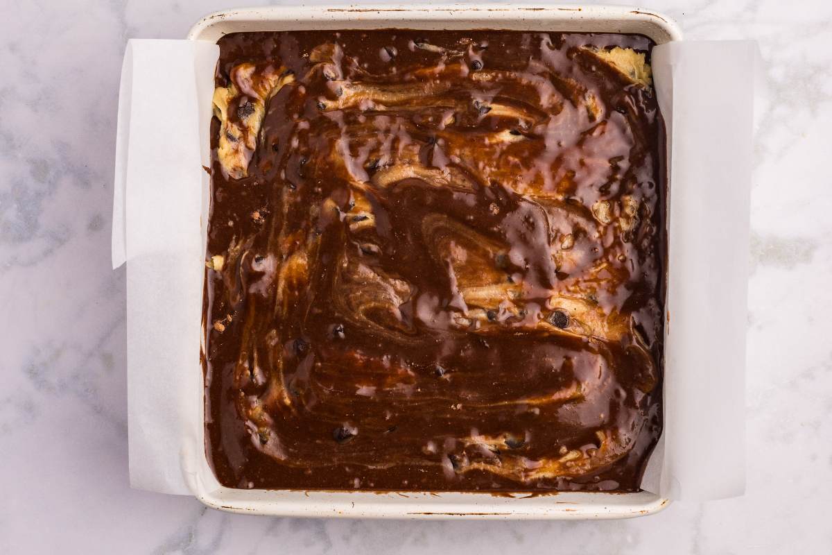 Unbaked brookie batter swirled in a white parchment-lined pan.