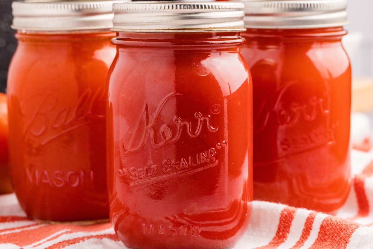 3 jars finished tomato sauce on striped towel.