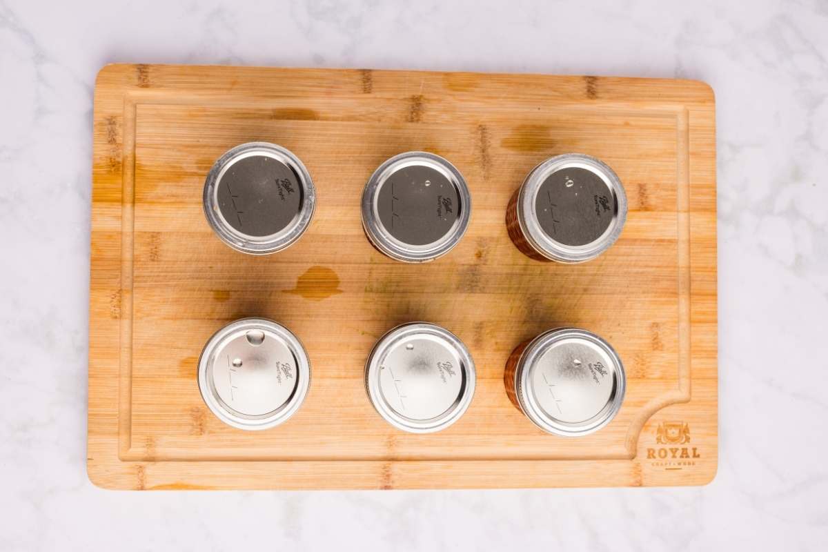 Six empty mason jar lids arranged on a wooden cutting board.