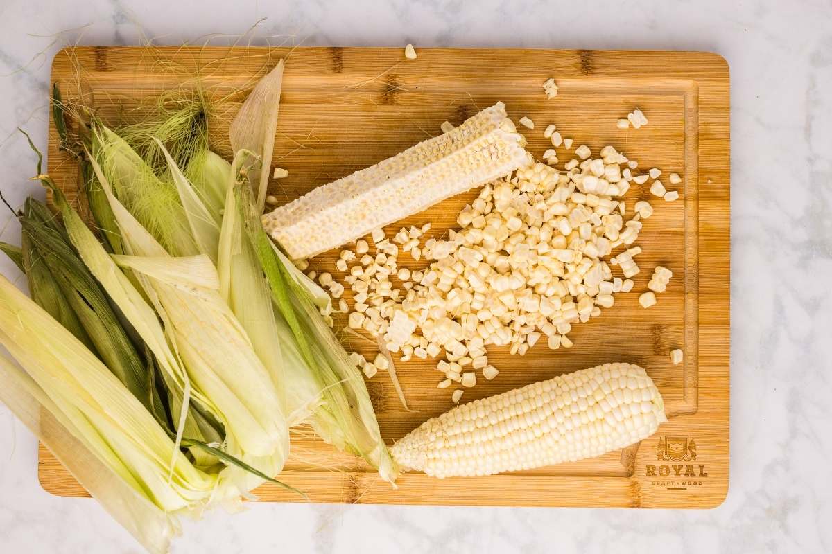 Corn cobs, husks, and kernels on a wooden cutting board.