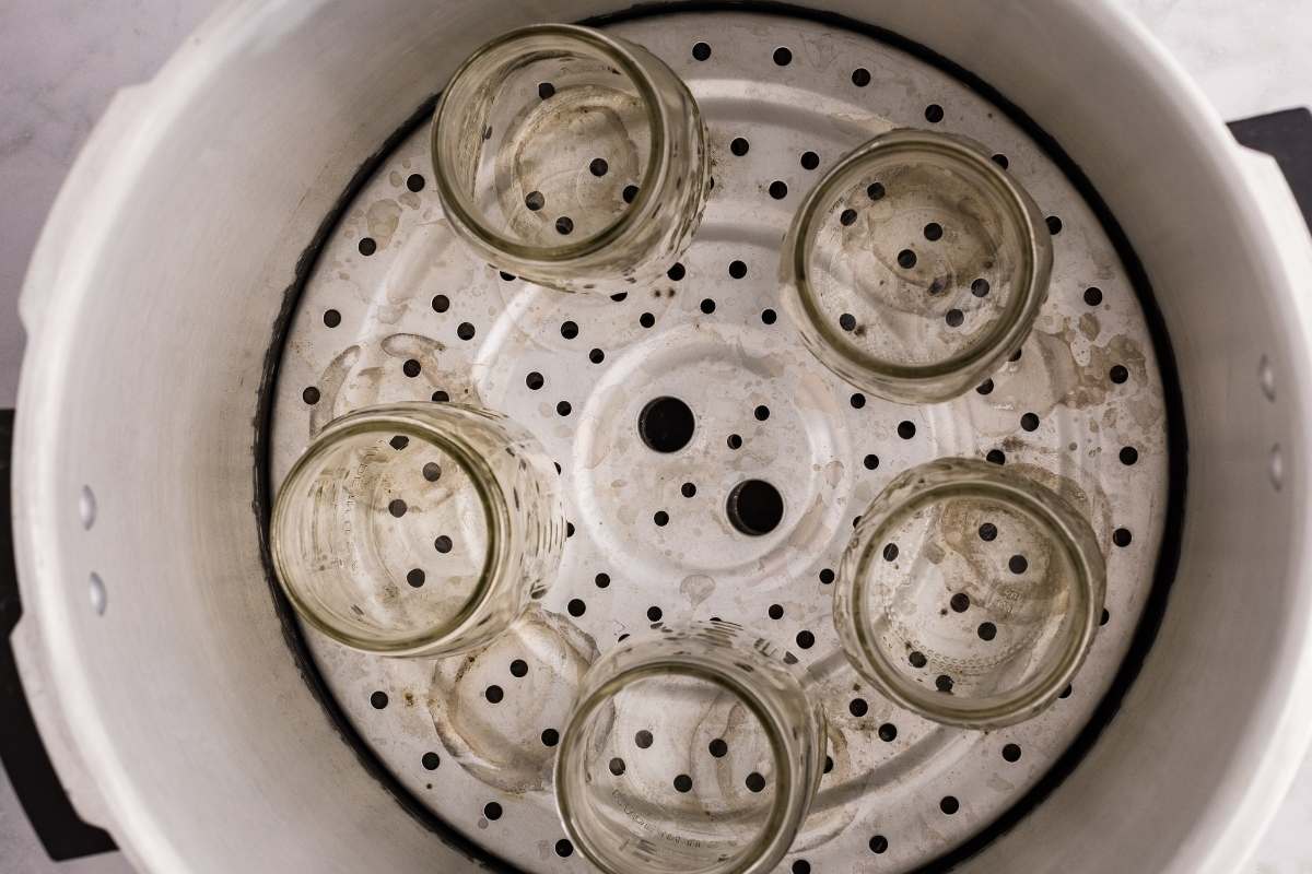 Five empty jars inside a pressure canner on a perforated rack
