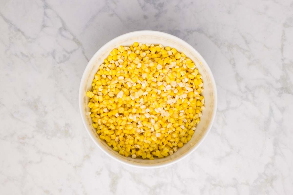 A large white bowl filled with cut corn kernels.