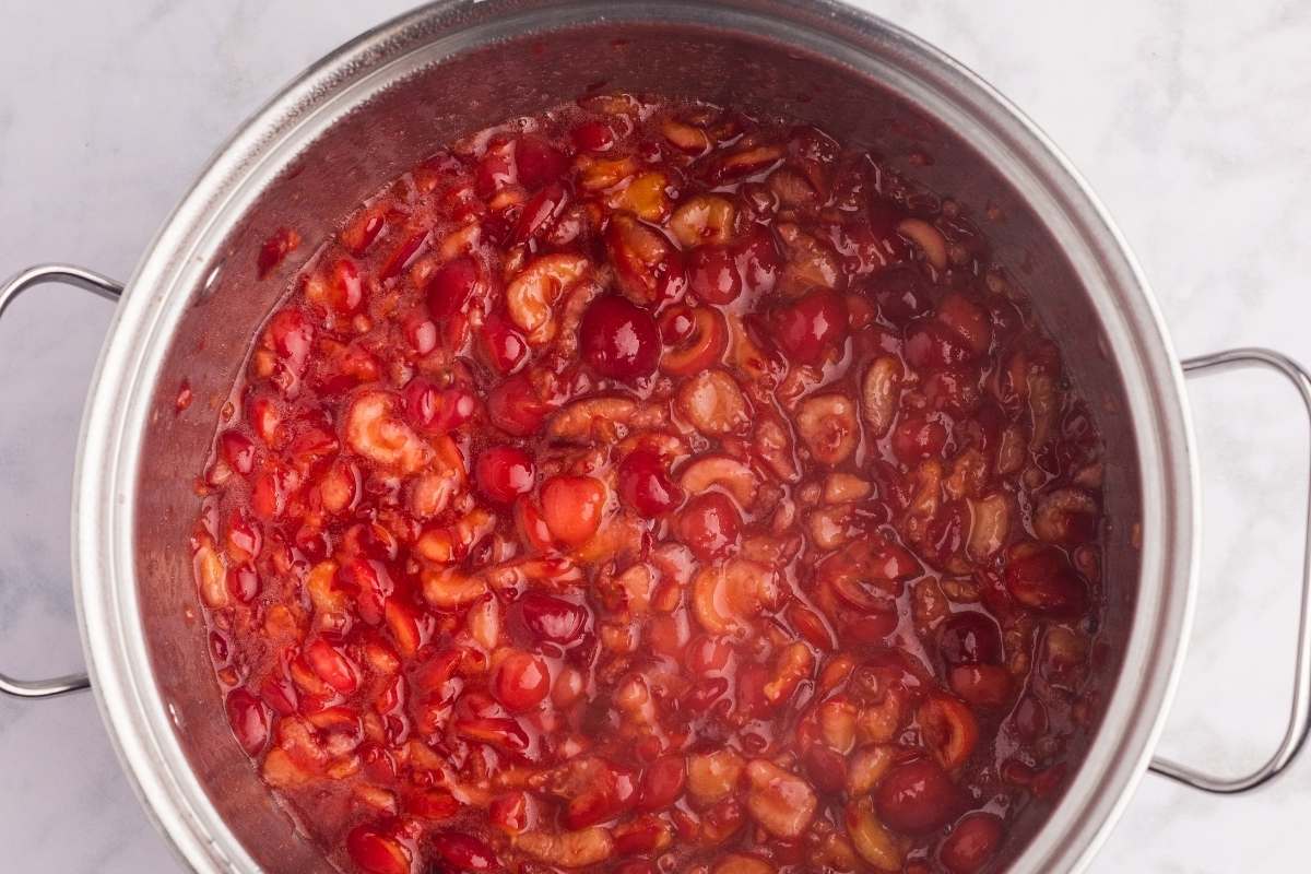Cherry jam mixture bubbling in a stainless steel pot.