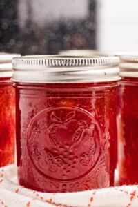 Glass jars filled with red cherry jam with metal lids.