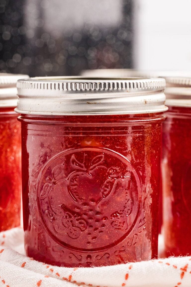 Glass jars filled with red cherry jam with metal lids.