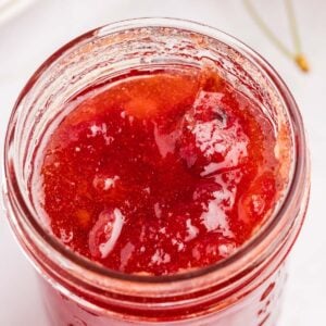 Red cherry jam in a glass jar viewed from above.
