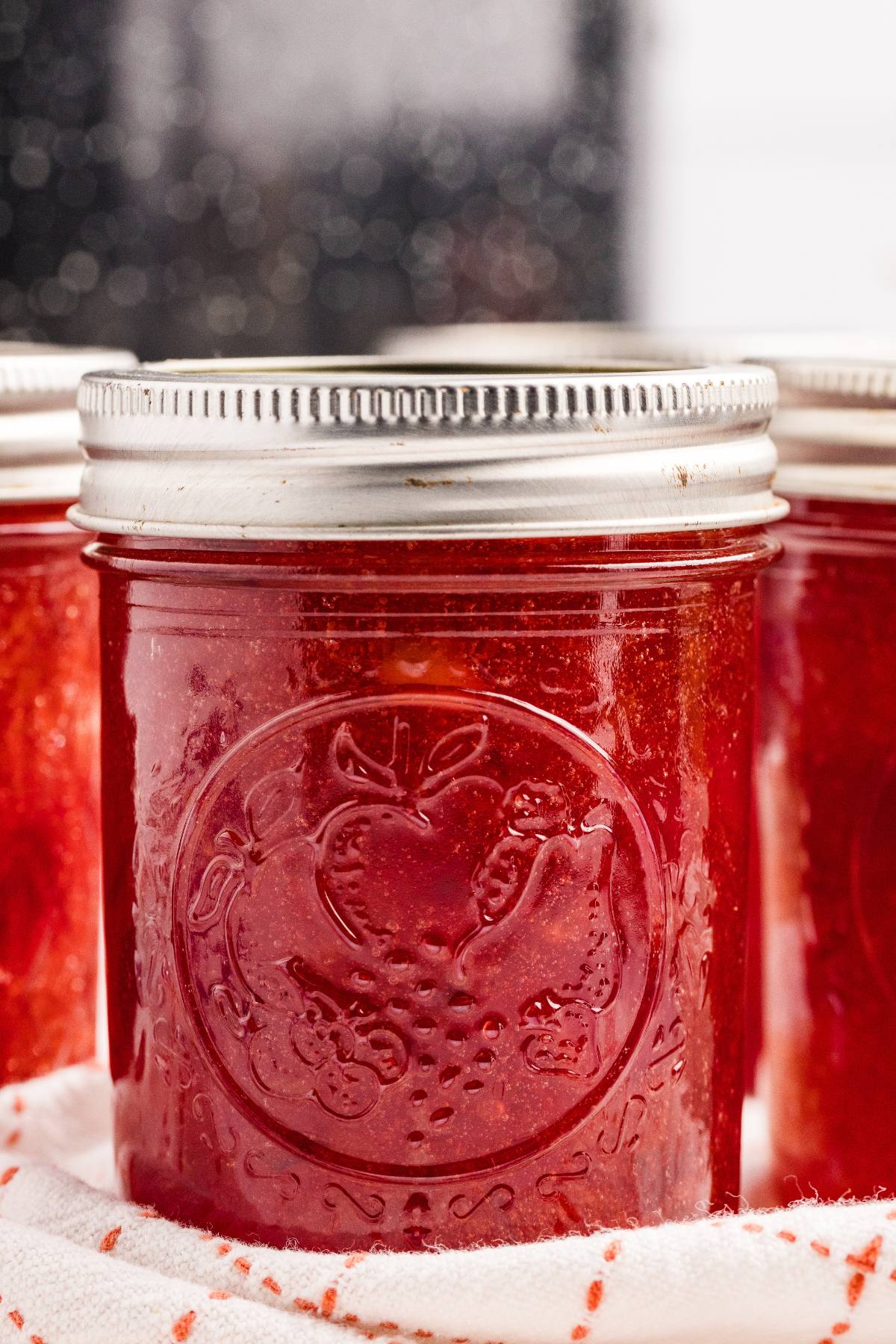 Glass jars filled with red cherry jam with metal lids.