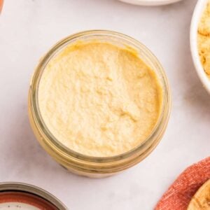 Jar of homemade yellow Dijon mustard with mustard seeds in bowls nearby.