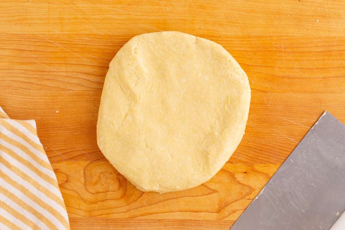 Round ball of pastry dough wrapped and chilled on cutting board.