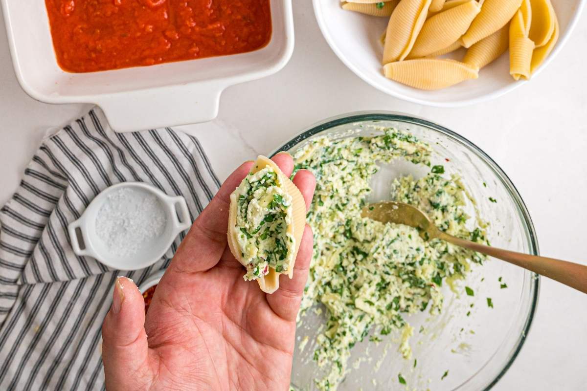 Hand holding a filled pasta shell over bowl.