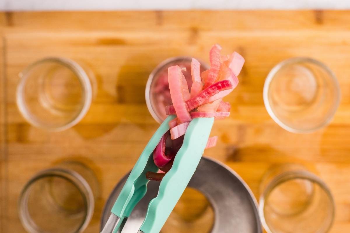 Tongs placing cooked onion strips into empty jar.