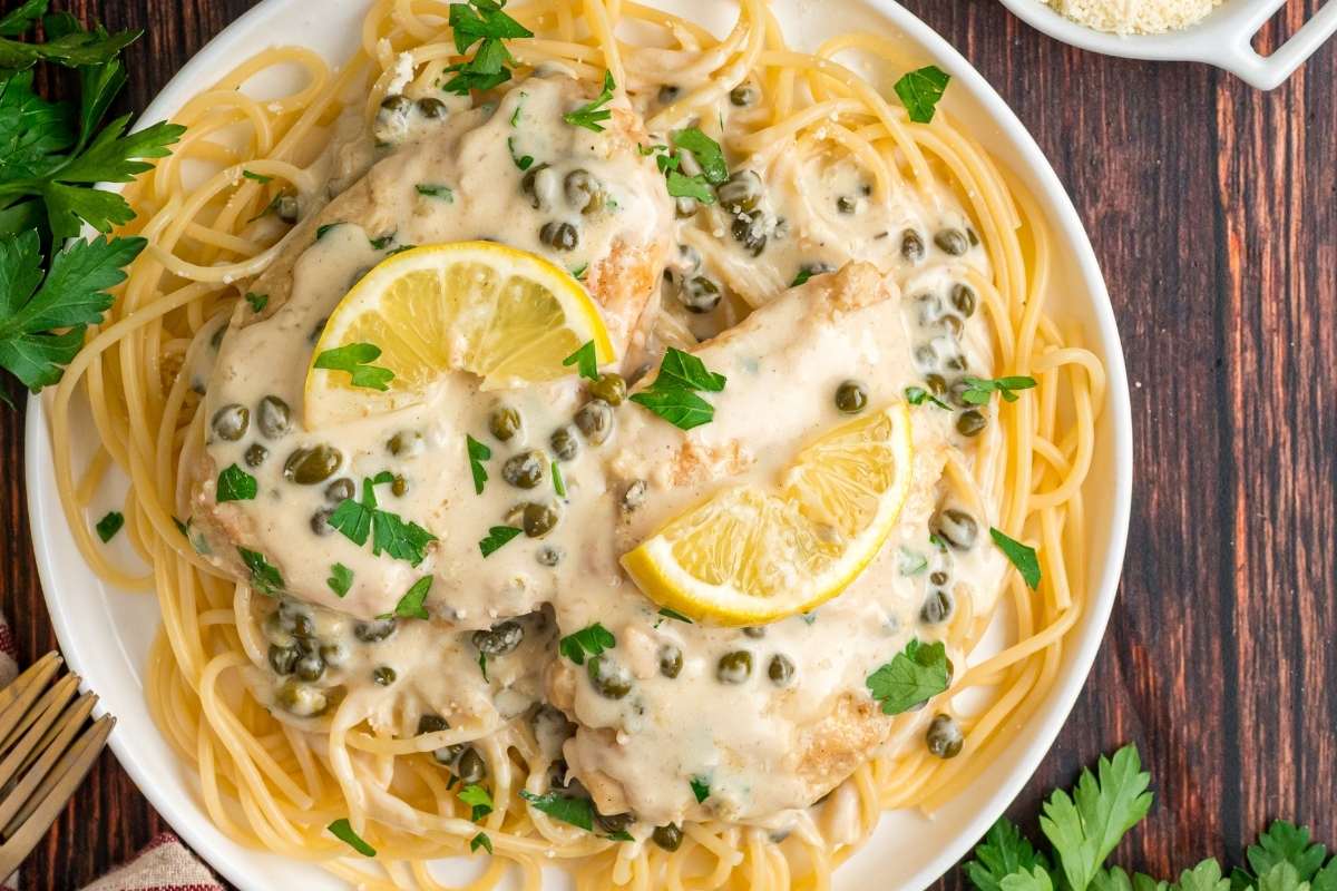 Creamy chicken piccata served over spaghetti on a white plate.