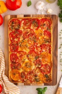 Whole baked tomato tart on wooden cutting board with fresh ingredients around.