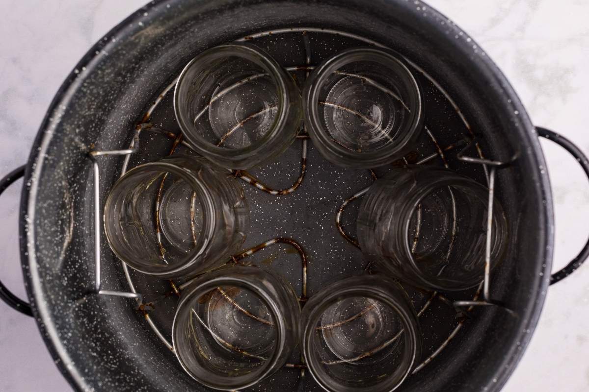 Empty canning jars warming inside water-bath canner rack.