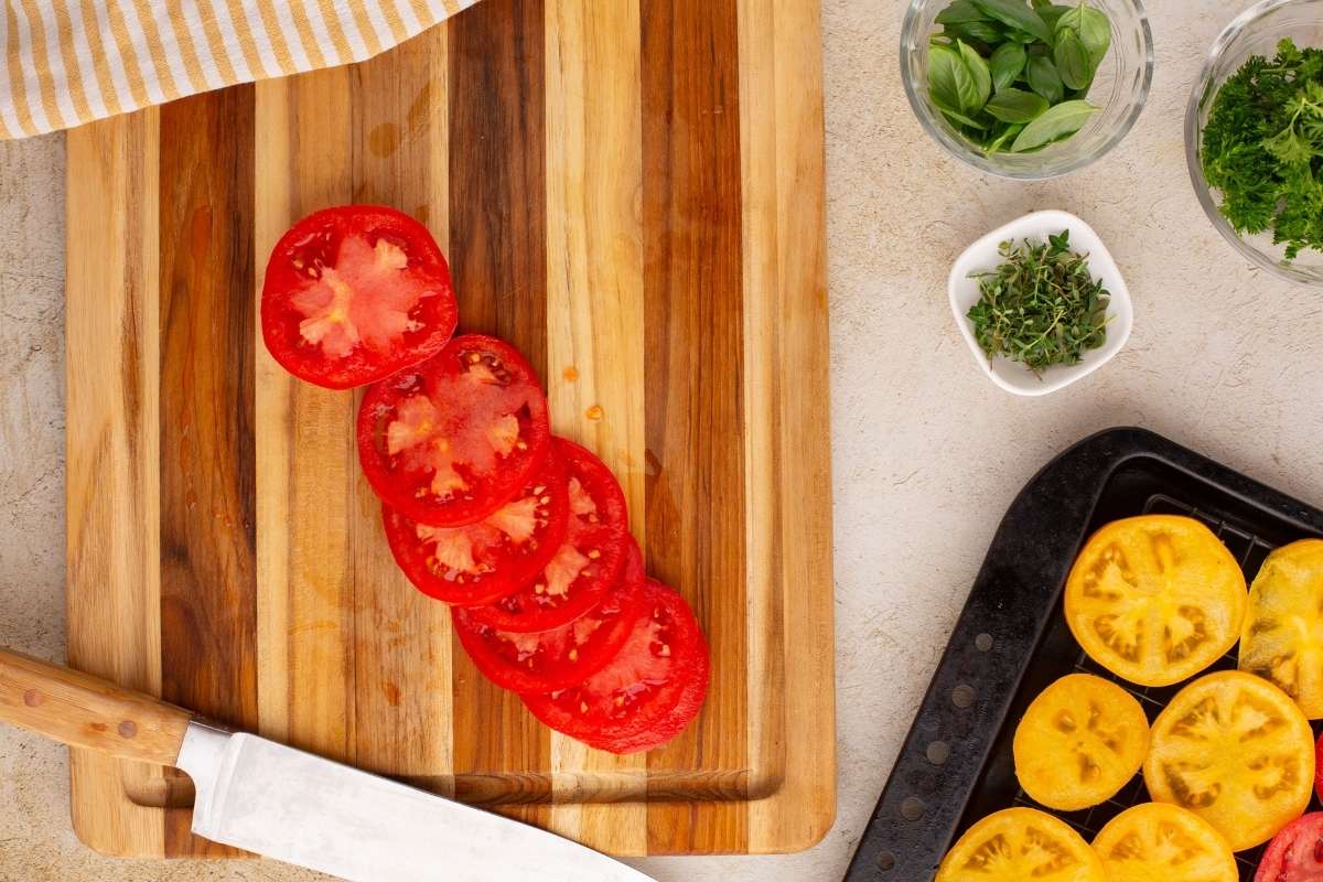 Sliced red tomatoes on cutting board with fresh herbs nearby.