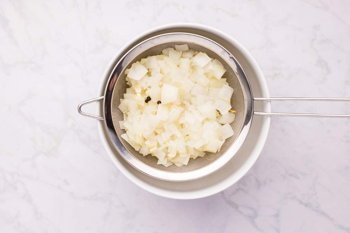 Fine mesh strainer with cooked onion mixture being strained into bowl.