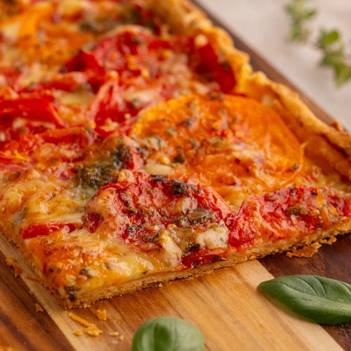 Slice of tomato tart with golden cheese and herbs on wooden board.