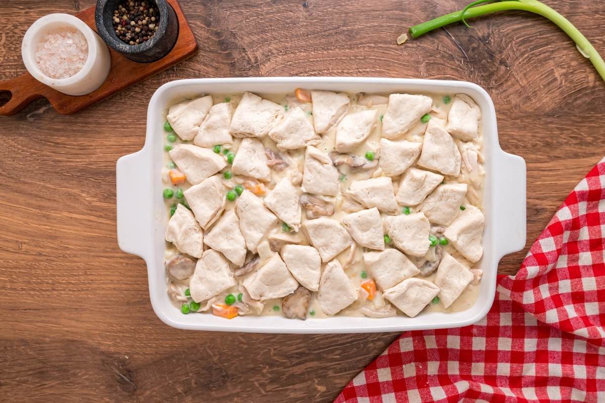 Unbaked casserole with raw biscuit pieces arranged on filling.