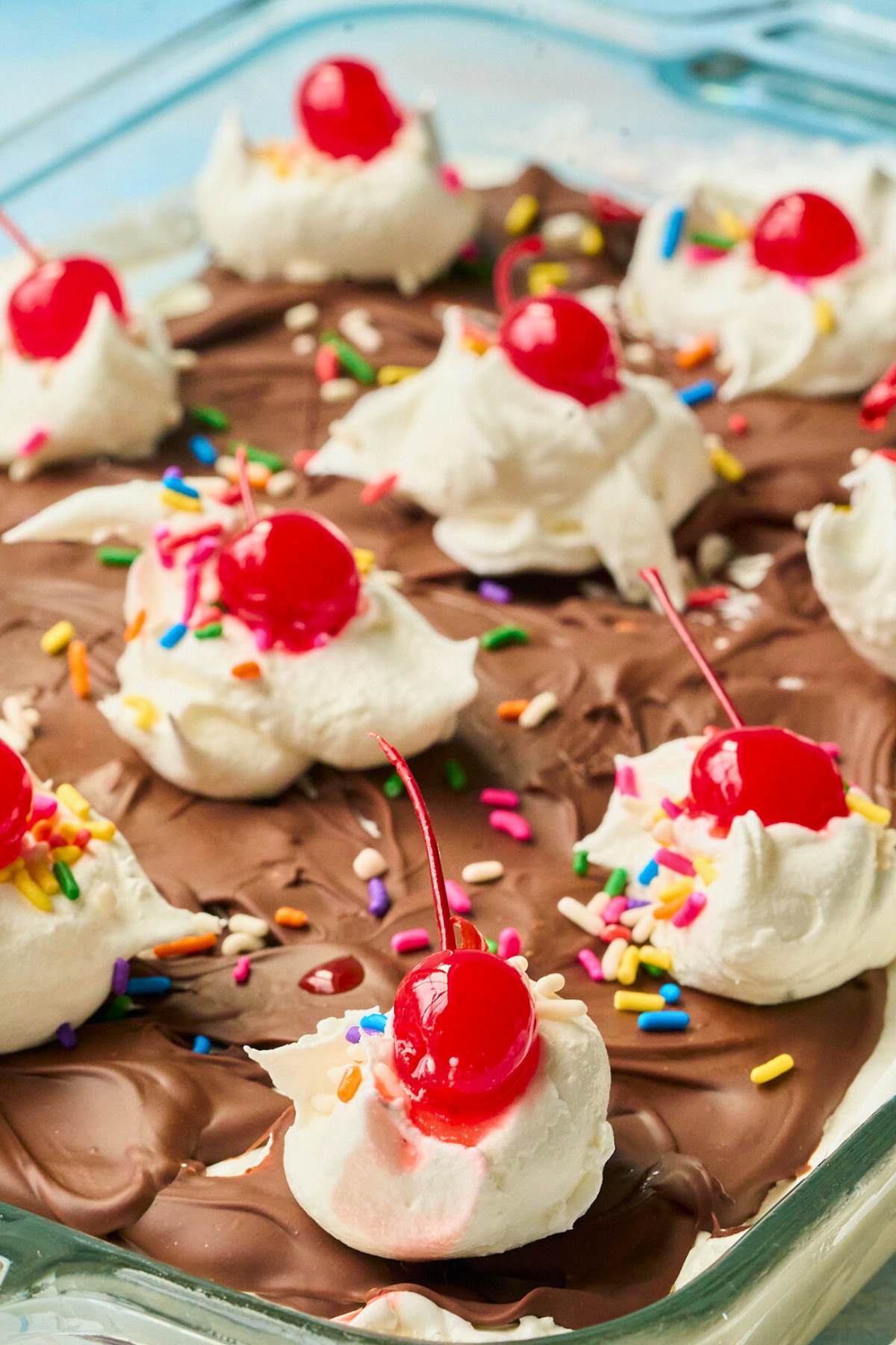 Overhead view of ice cream squares with chocolate, whipped cream and cherry toppings.