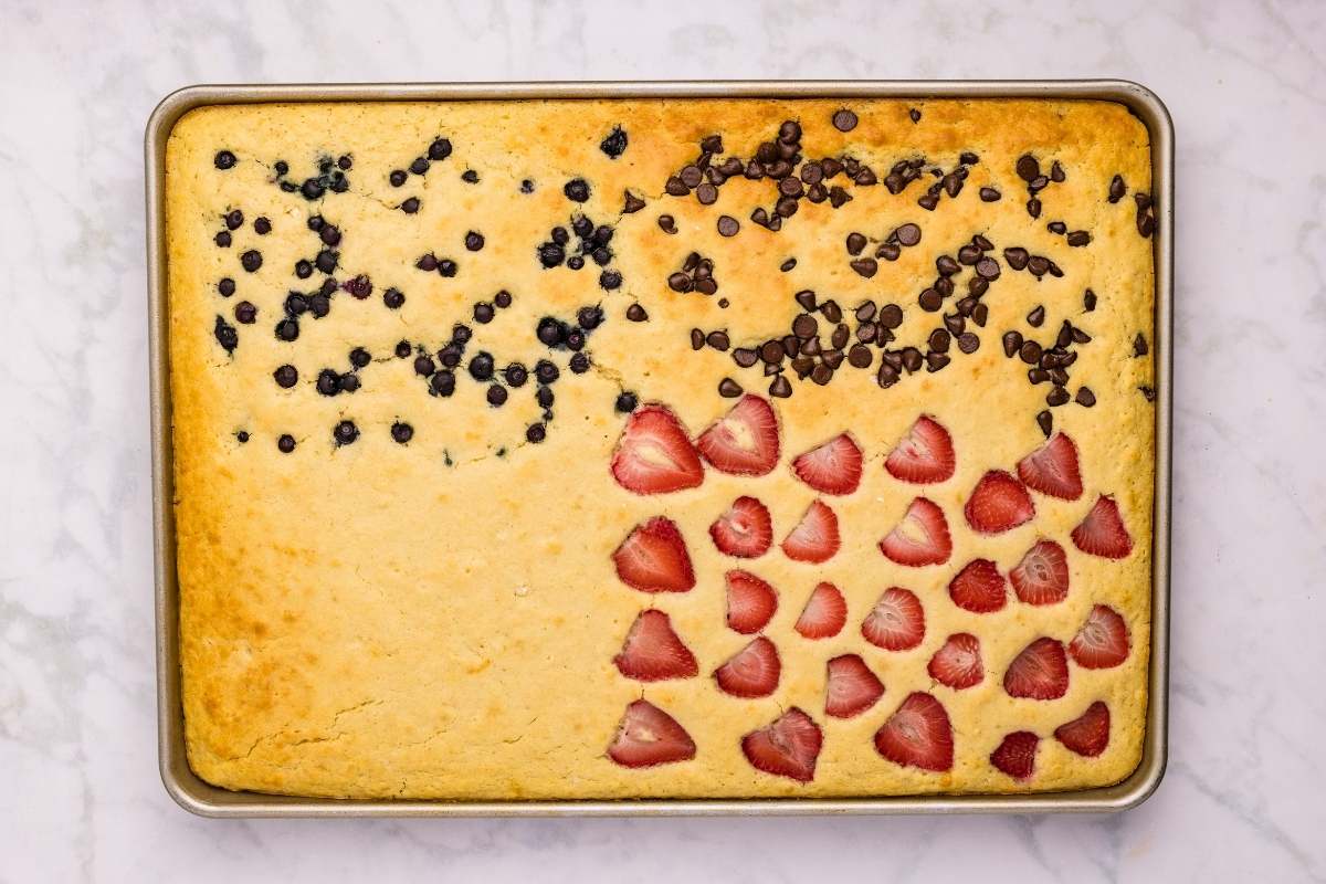Golden baked sheet pan pancakes with blueberries, chocolate chips, and sliced strawberries on top.