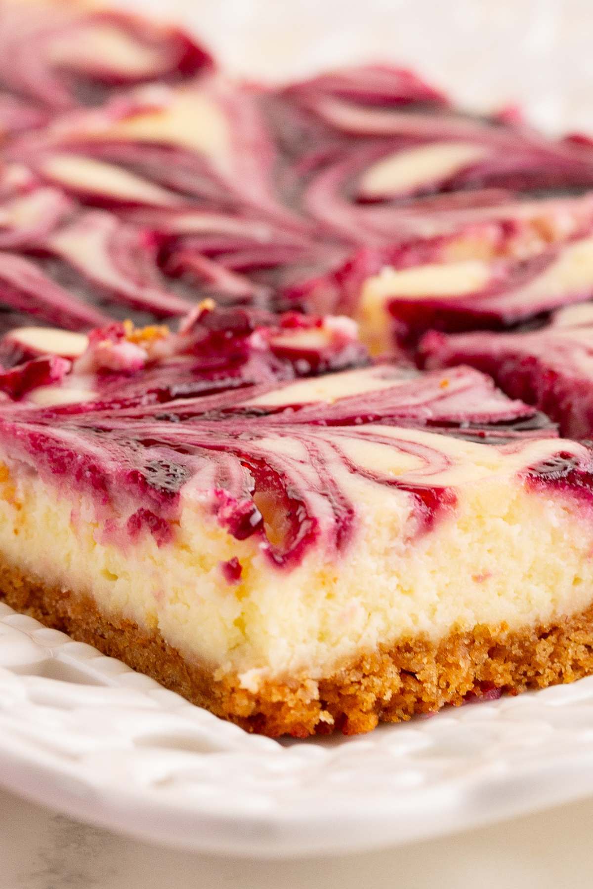  Blackberry cheesecake bars with swirled berry topping and graham cracker crust on white plate.