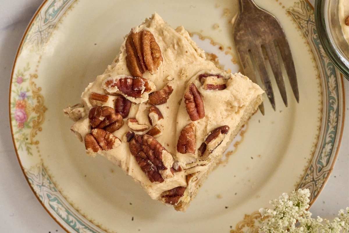 Square slice of spice cake with praline frosting and pecans on vintage plate.