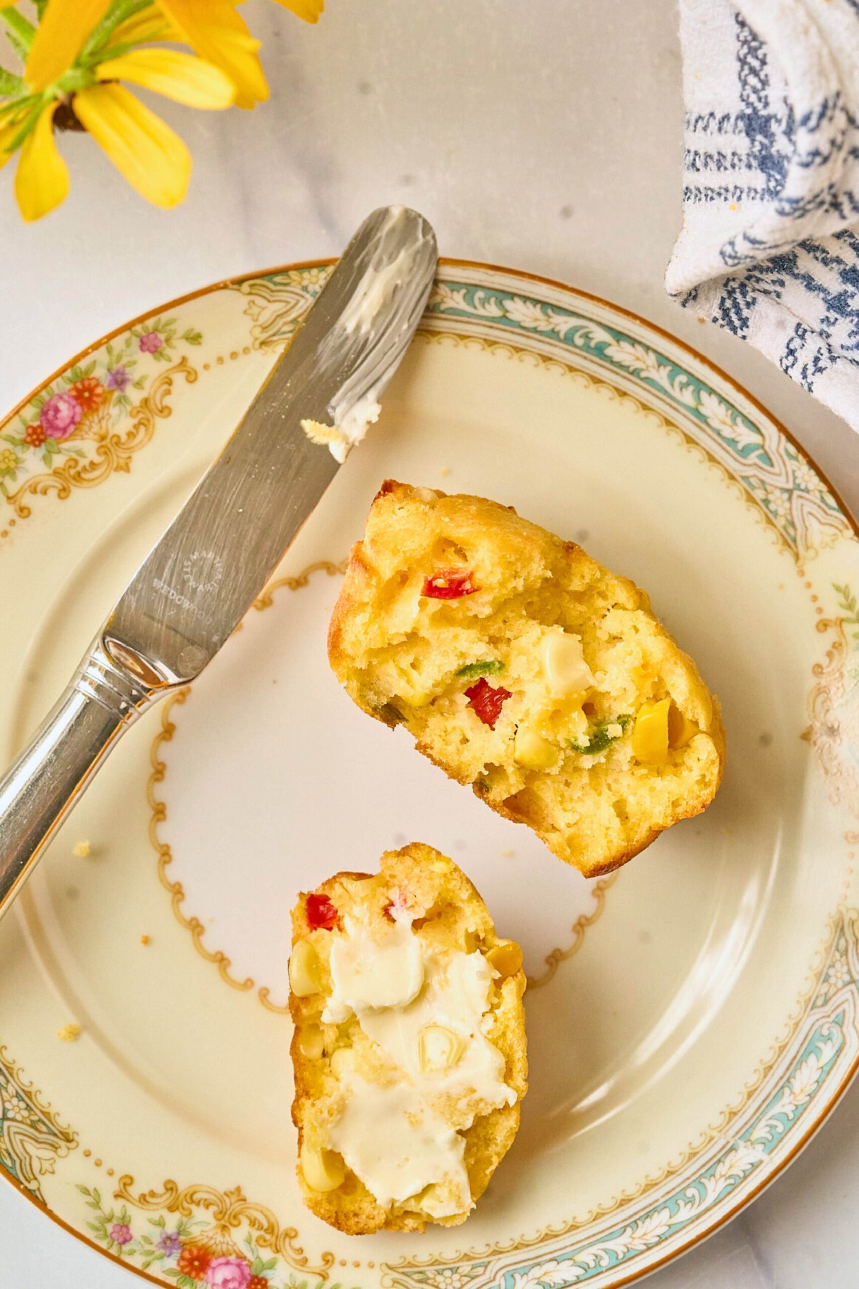 Cornbread muffin cut in half on a plate with butter and a knife.