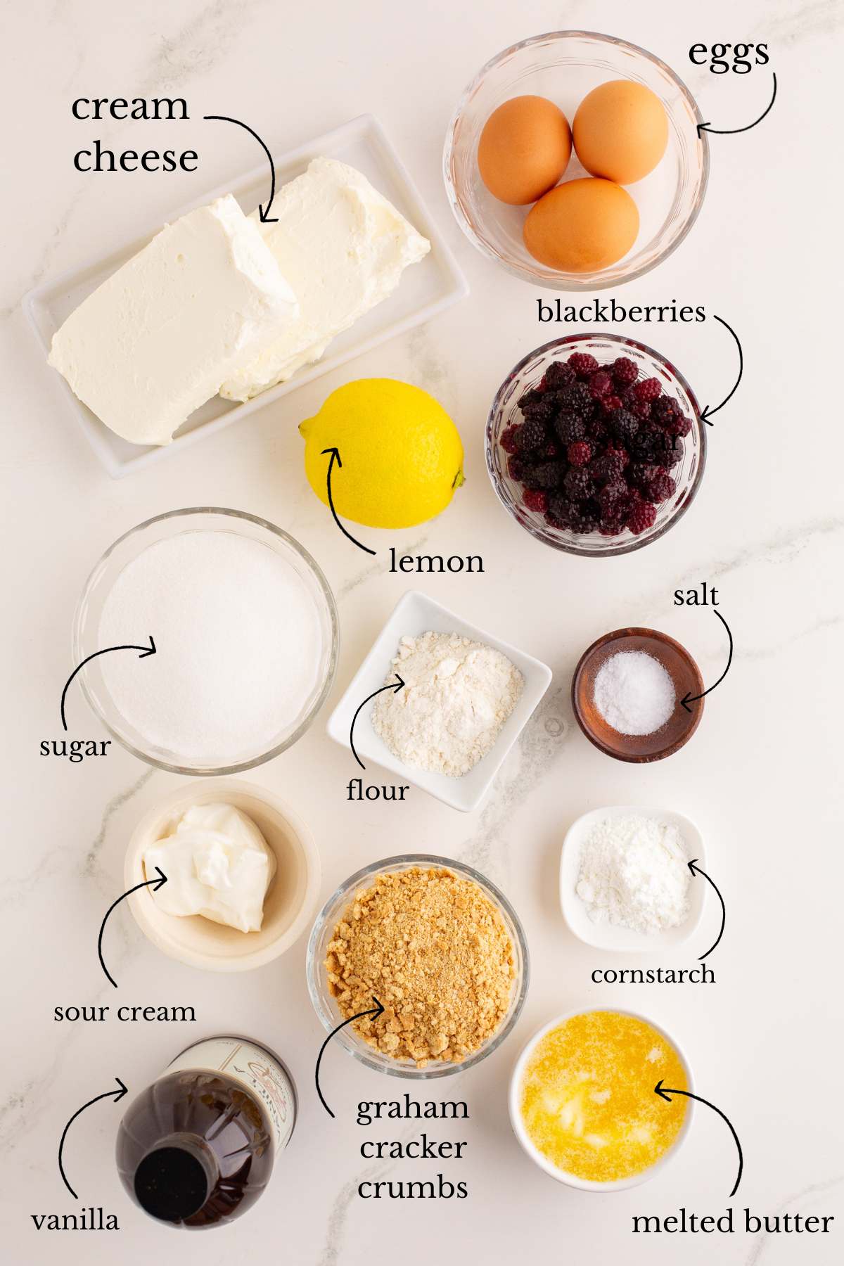 Ingredients for blackberry cheesecake bars laid out including cream cheese, eggs, and blackberries.