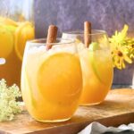 Two stemless wine glasses filled with autumn punch and cinnamon stick garnish.