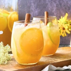 Two stemless wine glasses filled with autumn punch and cinnamon stick garnish.