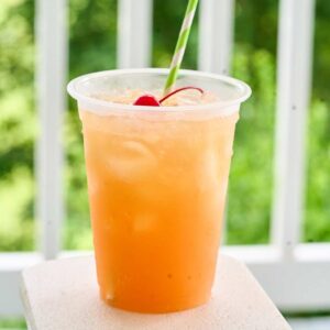 : Single glass of orange rum punch with cherry garnish and green striped straw.