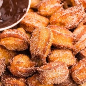 Golden brown churro bites with star shapes covered in cinnamon sugar with chocolate sauce.