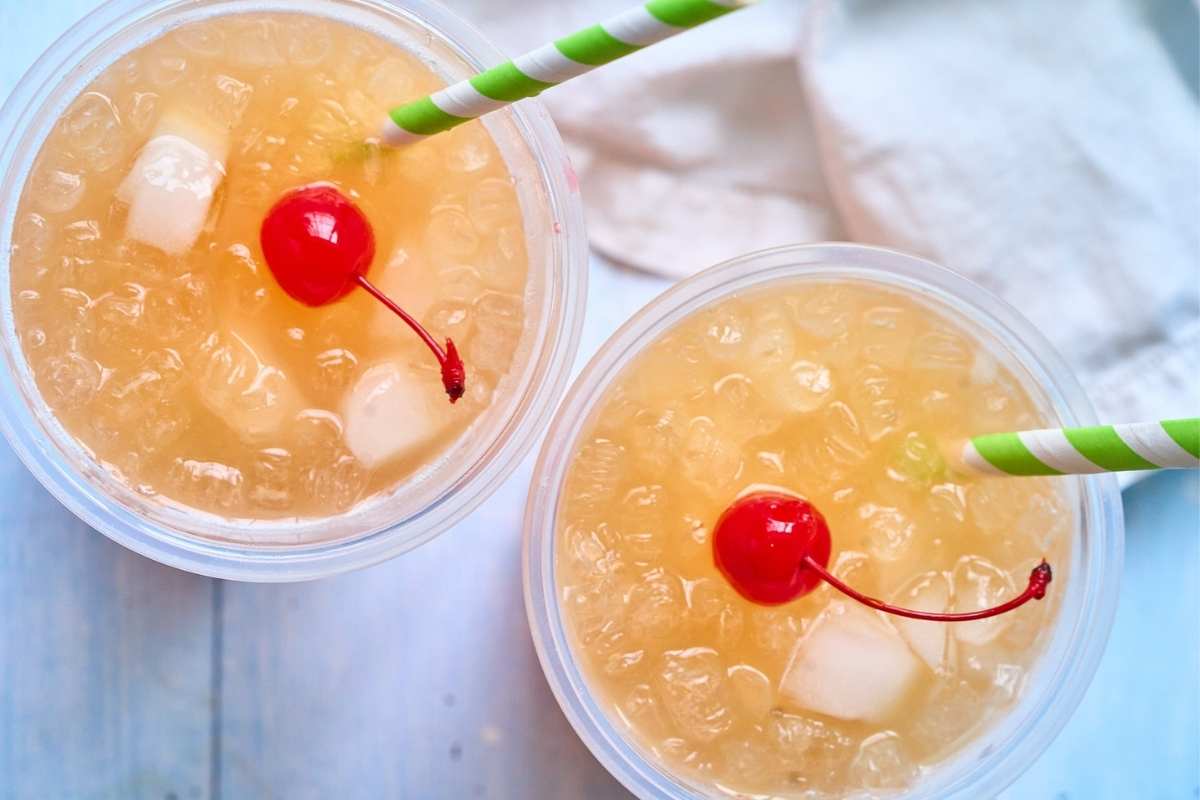 Two glasses of orange rum punch with ice, cherries, and green striped straws.