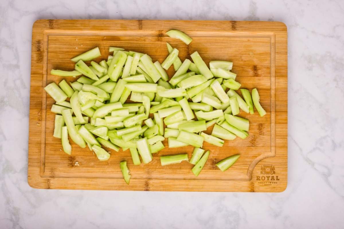 Peeled and cut cucumbers on a wooden cutting board.