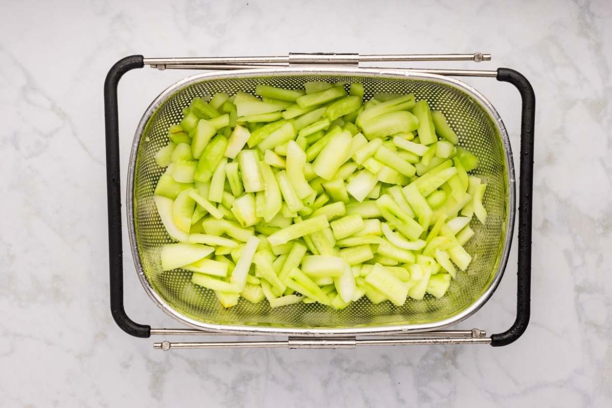 Cut cucumbers draining in a metal colander.