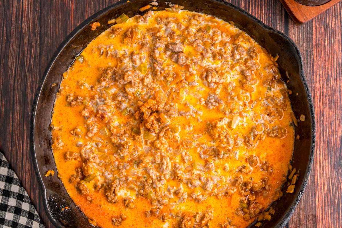 Milk simmering with meat and vegetables in skillet.