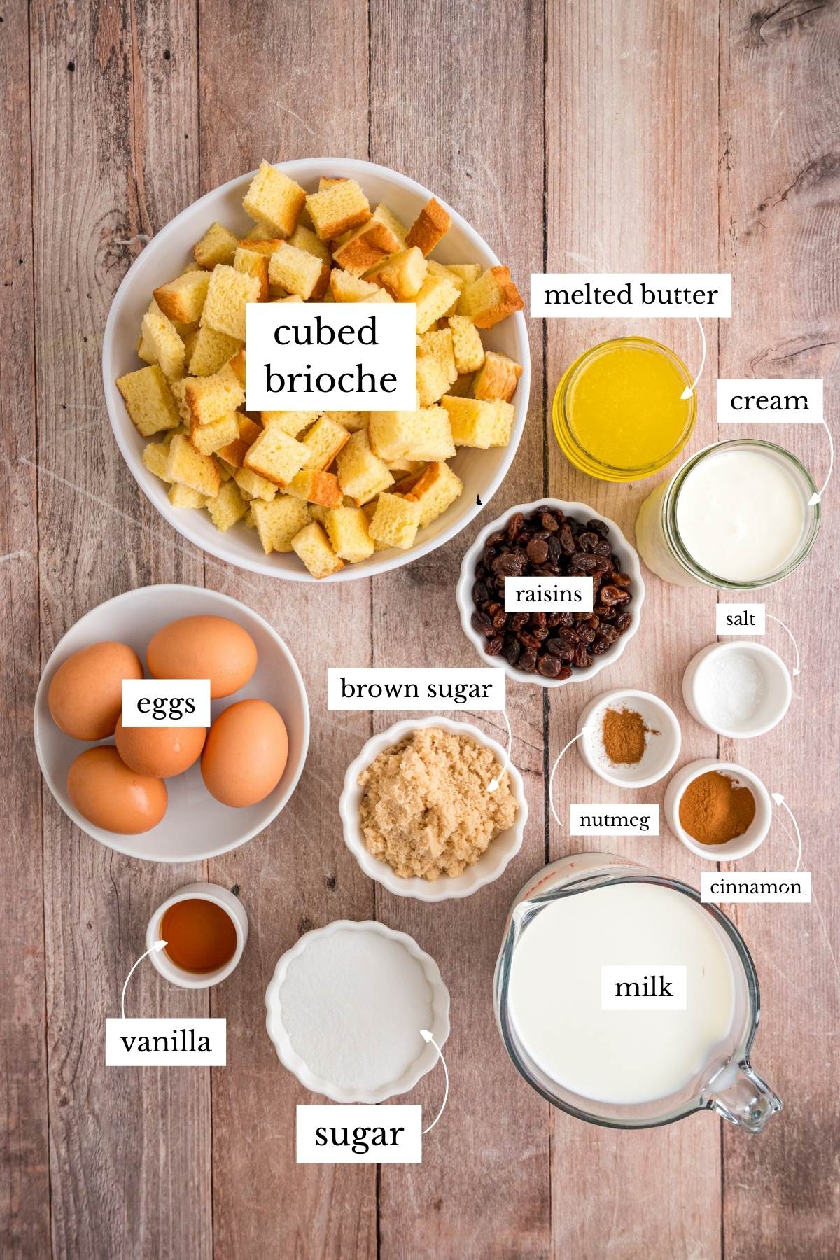 All bread pudding ingredients labeled and arranged on wooden surface.