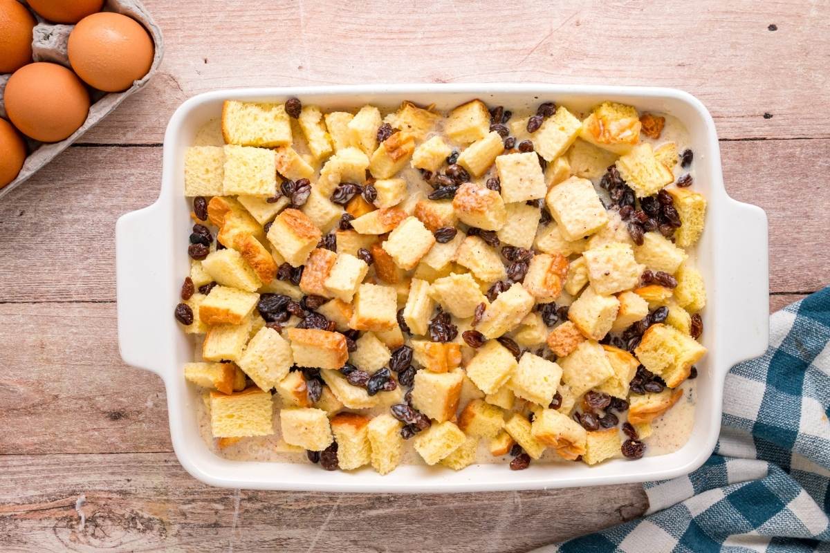 Bread cubes and raisins arranged in white baking dish before adding custard.