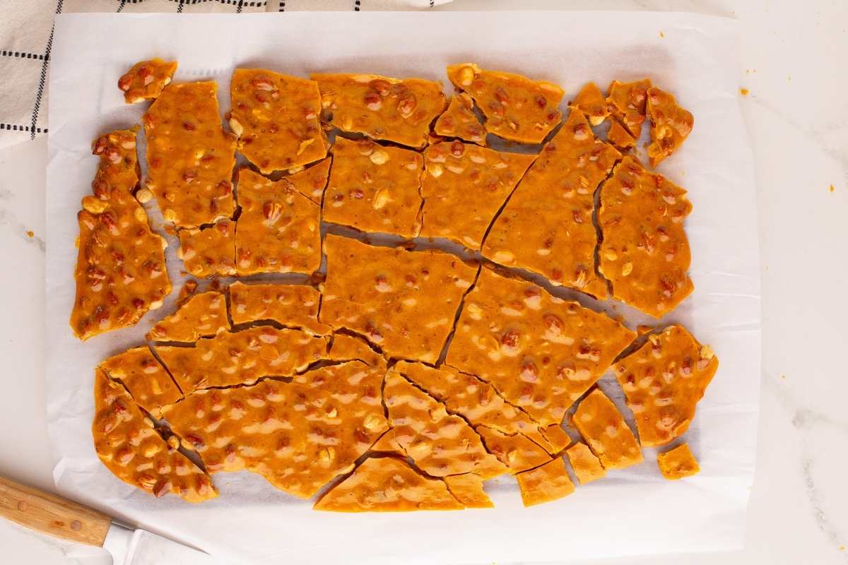 Broken peanut brittle pieces on parchment paper with a knife.