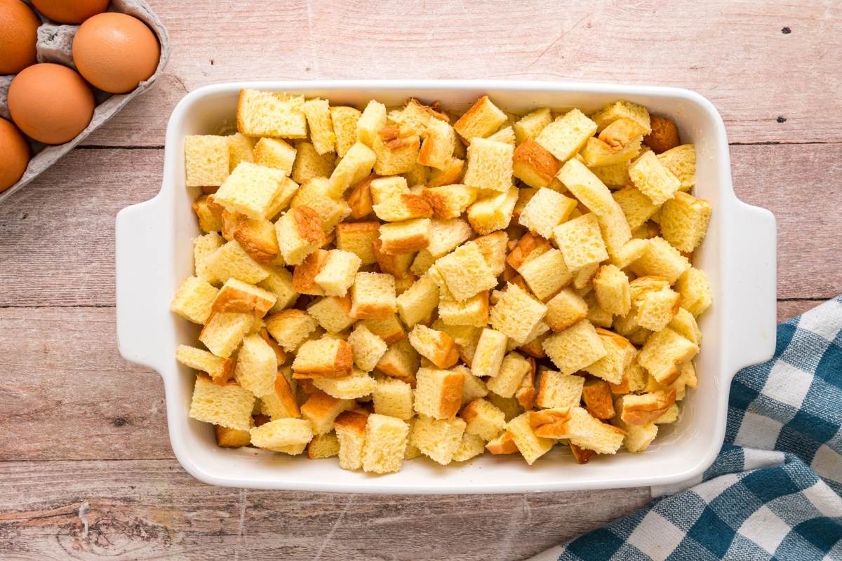 Cubed brioche bread pieces in white baking dish on wooden surface.